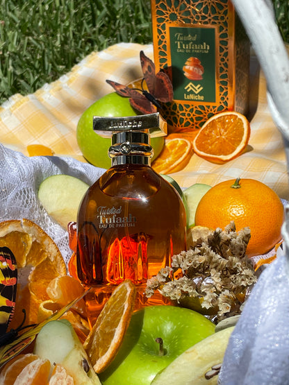 Bottle of Twisted Tulaah perfume surrounded by fruits and decorative elements on a table outdoors.